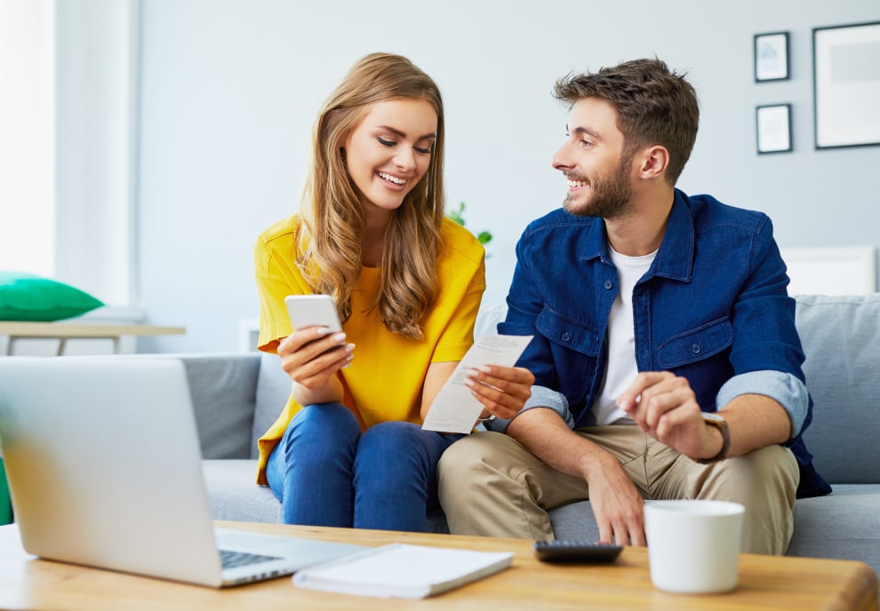 Happy couple looking at their phone and electricity bill